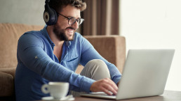 Young smiling man with headphones using laptop in his home